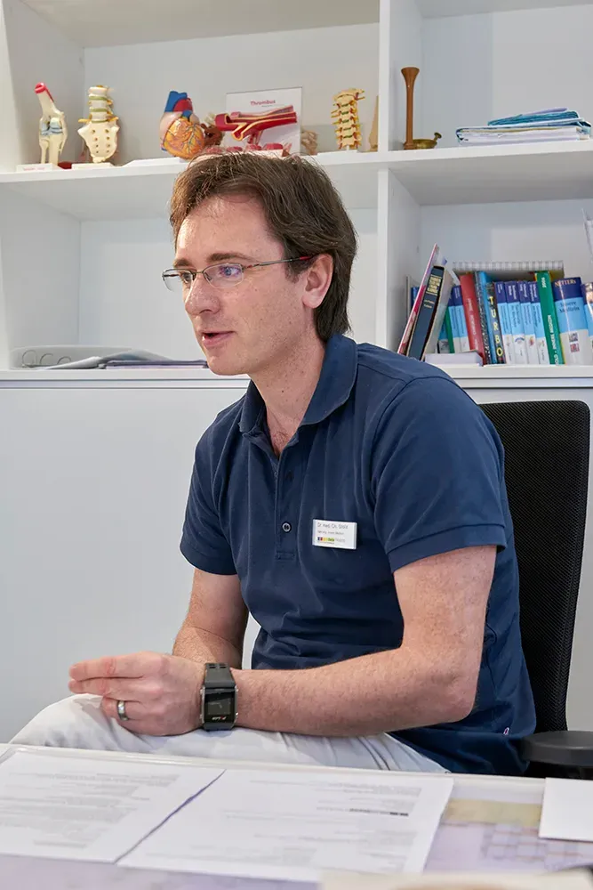 Dr. Christian Stolz sitzt an seinem Schreibtisch und erzählt